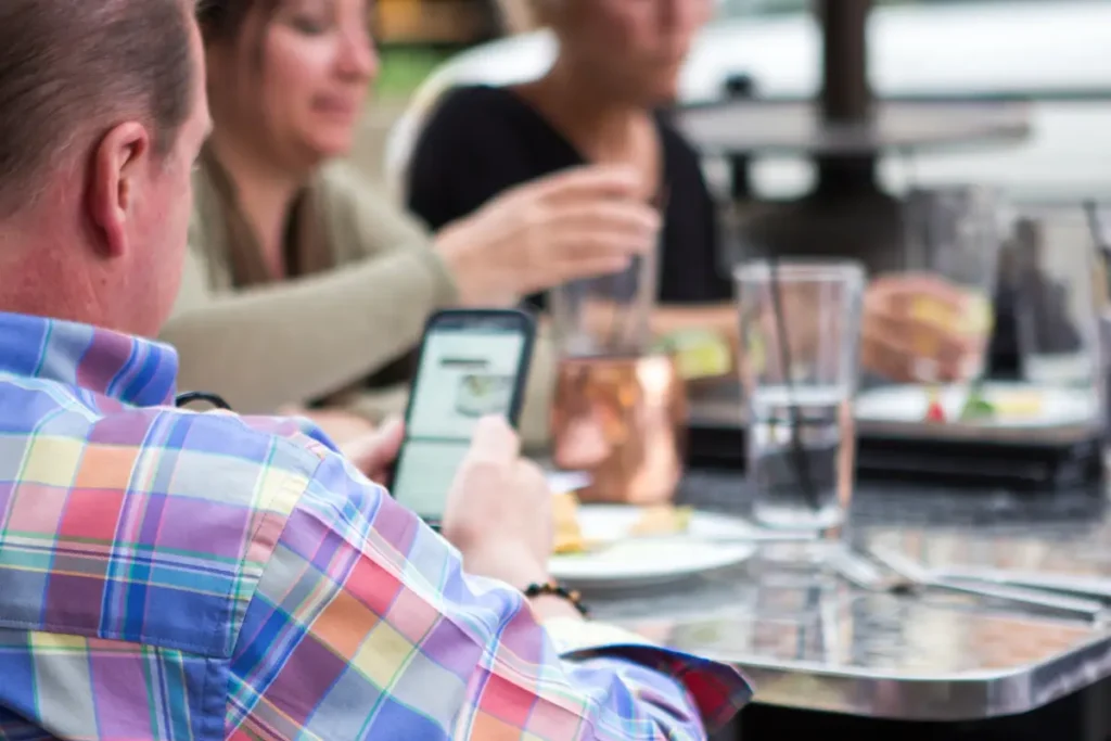 Cliente mirando el móvil en un restaurante mientras busca el menú, afectado por la carta pdf restaurante